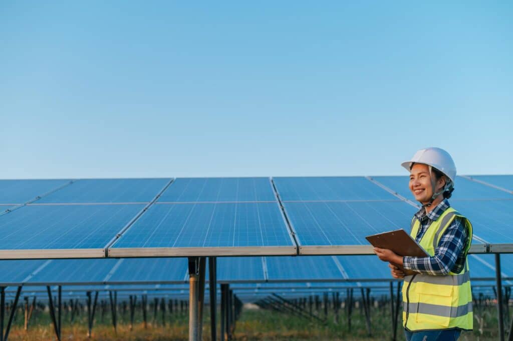 solar development with female worker with safety uniform holding clipboard standing in front of panels